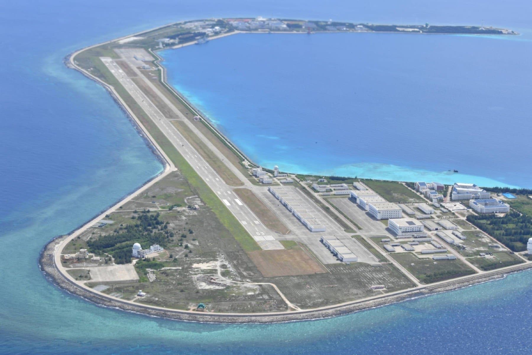 Aerial photograph of an island airfield, annotated in the manner of an intelligence read: a datum rule with station ticks, and three open squares marking the airstrip, the sheltered water on its north side, and the support area, each with a leader running down to a placard along the foot of the plate. The placard lists three courses open to the force holding the feature — A, assessed most likely, to reinforce and hold; B, to thin out and preserve; and C, assessed most dangerous, to operate from the feature.